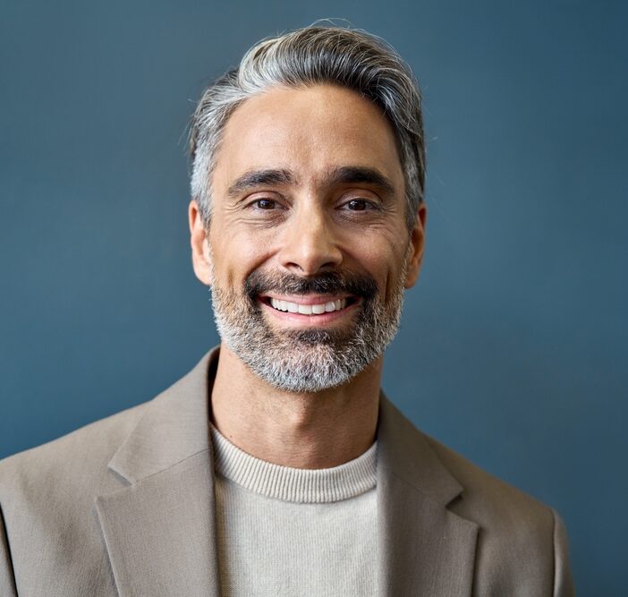 Smiling middle-aged man with gray hair in a neutral background, representing a satisfied dental patient